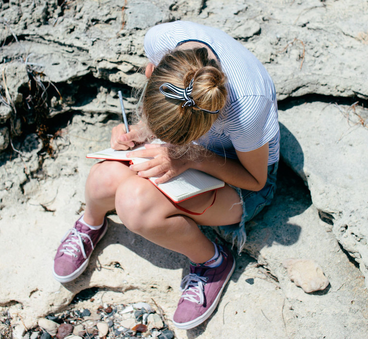 Girl writing on notebook sitting on a rock